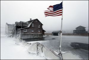 A tattered flag flies by a flooded yard along the shore in Scituate, Mass. today. A blustering winter storm that dropped nearly 2 feet of snow just north of Boston.