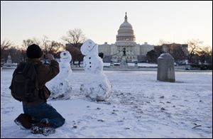 A man takes photos of snowmen with the Capitol in the background today.