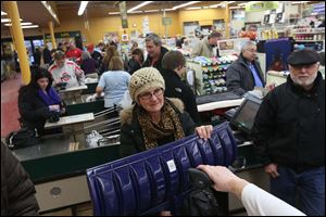 Kim Flowers of Maumee, center, with her new snow shovel, goes through the checkout at The Andersons in Maumee after picking up food for a friend. She left one store earlier because of the number of shoppers. 