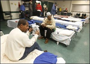 Howard Carrington, left, sits on a cot that he will sleep on for the night at St. Paul's Community Center in Toledo.