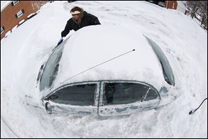 In an imagge made with a fisheye lens, Marguerite Johnston uncovers her car in Grosse Pointe, Mich. Michigan residents are preparing for diving temperatures as they dig out from more than 15 inches of snow in places.  