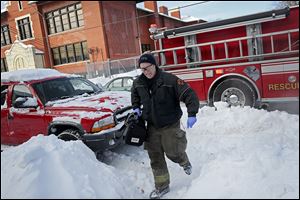 Toledo firefighter Bill Bruss wades through the snow to carry a medical pack into a home for an ill person Tuesday in South Toledo. The unusually cold weather and snow has forced firefighters to contend with more calls from people unable to reach hospitals and made their routes harder.