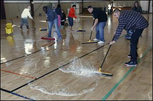Mario Rodriguez, right, is among about a dozen people who volunteered  to dry the gym floor  Wednesday at the Perrysburg Heights Community Center . The floor flooded during a frozen water pipe break.