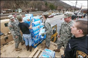 Members of the West Virginia Army National Guard, plus a member of the Belle Police Department and a volunteer, move emergency water from a military truck to a forklift in Belle, W.Va.