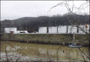 Workers, left, inspect an area outside a retaining wall around storage tanks Monday where a chemical leaked into the Elk River at Freedom Industries storage facility in Charleston, W.Va. 