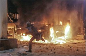 A protester throws a stone at a burning police bus in Kiev, Ukraine, on Sunday. An opposition leader who called for calm was sprayed with a fire extinguisher.