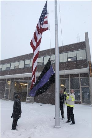 Deputy Toledo Fire Chief Brian Byrd, acting Deputy Chief Richard Syroka, and Battalion Chief John Kaminski lower the U.S. flag to half staff, and raise a funeral flag, at Toledo Fire and Rescue headquarters on North Huron Street,  early today in honor of firefighters Stephen A. Machcinski and James A. Dickman who were killed Sunday.