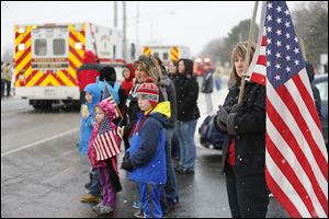 Kim Cowie of Sandusky, with the U.S. flag, joins others in front of Perkins Township Fire Station 2 to wait for the procession as it moves toward the cemetery.