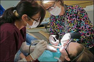 Heather Blair, a certified dental assistant, left, and certified hygienist Kelly Bardwell, right, clean the teeth of Lindsay Roof, 13, during the Give Kids a Smile program at Owens Community College’s dental hygiene clinic. Two other sites offered the free services on Friday to about 450 children.