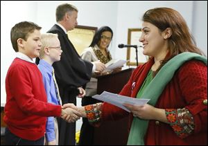 Bahija Gouriny, formerly of Morocco, shakes hands with Waterville Primary School third grader Aidan Funk after receiving her certificate of citizenship during a naturalization ceremony at the Browning Care Center in Waterville.