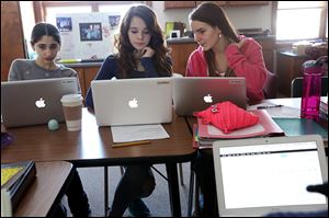 Leen Yassine, 13, left, Parker Caesar, 13, center, and Libby Stupica, 14, discuss stock prices while selecting companies to add to their portfolio at Toledo’s West Side Montessori school.