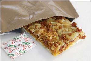 A slice of prototype pizza, in development to be used in MRE's — meals ready to eat, sits in a packet next to a smaller packet known as an oxygen scavenger, left, at the U.S. Army Natick Soldier Research, Development and Engineering Center in Natick, Mass. 