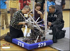 Mentor Skip Mozena, left, of Dana Holding Corp., repairs a robot that picks up and kicks a ball while Joe Neyhart, a senior at Toledo Technology Academy, explains the process to Romules Durant, superintendent of Toledo Public Schools.