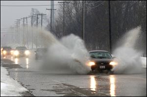 Plumes erupt from cars passing through water on Sylvania Avenue near Centennial Road in Sylvania Township, the result of melting snow and rainfall.
