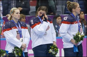 Megan Bozek of the United States (9) wipes a tear as she stand with Monique Lamoureux of the United States (7),  and Meghan Duggan of the United States (10) during the medal ceremony for the women's ice hockey tournament Thursday.