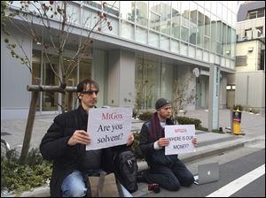 Bitcoin trader Kolin Burges, right, of London and an American counterpart hold signs during a sit-in in front of the office tower housing Mt. Gox in Tokyo. Reports say the major bitcoin exchange suffered catastrophic losses, handing the virtual currency a setback in its quest for legitimacy.