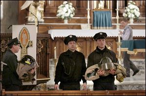 Toledo firefighters carry two fire jackets, boots, and helmets out of the parish during a Catholic Mass at the Historic Church of St. Patrick. The Mass on Wednesday marked the end of the one-month Catholic mourning period for Toledo firefighters James Dickman and Stephen Machcinski.