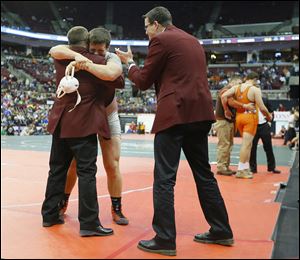 Genoa junior Jay Nino hugs assistant coach Dave Wlodarz as head coach Bob Bergman applauds after Nino beat New Paris National Trail’s Ben Sullivan to win the Division III 220-pound state title — his 65th victory, an Ohio record for a season.