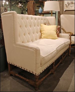 A tufted high back settee with exposed wood legs and stretchers is from the Donny Osmond Home Collection. 