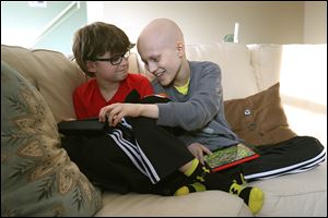 Gavin Boggs, right, jokes with his brother, Zachary, as they play a game on their iPads together at their home in Rossford.