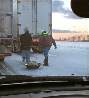 Two men pull a sled containing meals and water to stranded motorists, as seen through the windshield the vehicle of Maureen Dixon of Cleveland. She was stuck for seven hours in the traffic jam caused by the pileup on the Ohio Turnpike on Wednesday.