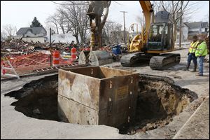 Construction workers excavate a sinkhole that opened up Tuesday on Fernwood Avenue near its intersection with North Detroit Avenue in Toledo. The hole was originally about 10 feet wide, but crews enlarged it in an effort to determine what caused the sink-hole. When they were done, the hole measured about seven feet deep and about 15 feet wide.