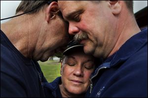 Darrington Fire District 24 volunteer firefighters, Jeff McClelland , left, Jan McClelland, center, and Eric Finzimer embrace each other Wednesday in Darrington, Wash., after saying a prayer for the victims and survivors of the massive mudslide. 