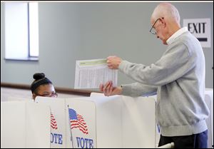 Poll worker John Flahie, right, helps first time voter Tyesha Fleming, left, 18, from Toledo, understand the paper voting system during the first day of voting at the Lucas County Early Vote Center.