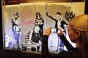 A woman photographs a section of restored wall graffiti artwork by famed street artist Banksy, as it is put on display to the public, today in London.