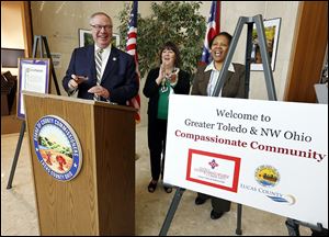Toledo Mayor D. Michael Collins smiles after he and Lucas County Commissioner Tina Skeldon Wozniak, back left, and  Paula Hicks-Hudson, Toledo City Council president, right, signed the Charter for Compassion in the lobby of One Government Center.