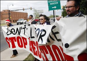 John Walters, Jana Lewis-Harkins, Fannie Bates and Aaron Baker, from left, hold a banner during a protest at the Governor's Mansion in Oklahoma City Tuesday.