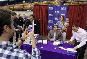 Justin Weaver, left, of Owensboro, Ky., takes a photo of Kentucky NCAA college basketball coach John Calipari, sitting, and Corey Millay and her daughter Adalyn, 2, at a book signing in Owensboro, Ky.