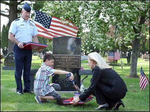 Myles Eckert, 9, shovels dirt from the grave of his father, Sgt. Andy Eckert, into a vessel held by Mary Robinson of the Patriot Soil Project as Lt. Col. Frank Dailey looks on at Whitehouse Cemetery.  Sergeant Eckert died while serving in Iraq nine years ago on Thursday.