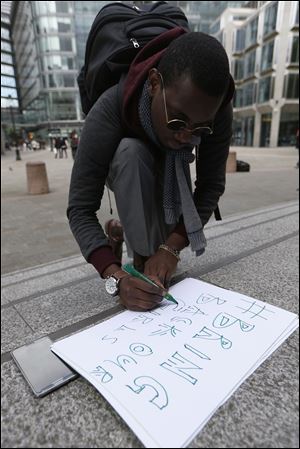 Nigerian student Caleb Udeoha writes out a placard  today in support of the campaign for the release of the kidnapped girls in Nigeria, outside Westminster Cathedral in London.