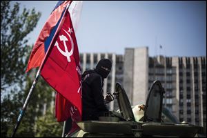 A masked pro Russia man is seen atop an APC flying a Russian flag, top, and a Donetsk People's Republic flag, as it stands in front of the occupied administration building today in Donetsk, Ukraine.