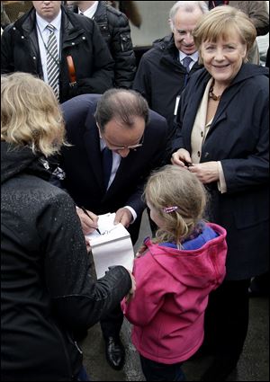 German Chancellor Angela Merkel, right, smiles as President of France Francois Hollande, center, gives an autograph to 6 years old tourist Hanna during a visit today in northern Germany.