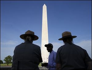 Park Service employees stand watch as visitor Roman Tanner, center, walks away with his Washington Monument ticket, which are distributed at on a first-come basis at the Washington Monument today ahead of a ceremony to celebrate its re-opening.