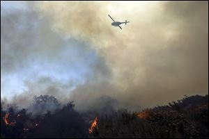 A helicopter flies over burning vegetation as it nears homes Wednesday in Carlsbad, Calif