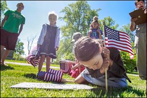 Molly Baldwin, 8, leans in to  place a  flag at Historic Woodlawn Cemetery in Toledo on Friday. She is joined by siblings, Isaac, 13, left, Margaret, 5, Mark, 6, behind Molly in a cap, and Gabriel, 15, who holds Josie, 2, on his shoulders. Placing the flags has become a tradition for the Baldwins and their dad, Anthony Baldwin, right.