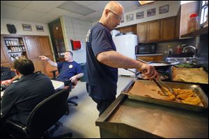 Firefighter John Martin makes a Friday fish fry for the other members of Fire House 7 on 2155 Franklin St. Firefighter Mike Lester, left, jokes around at the kitchen table. But when the alarm rings, the meal is over.