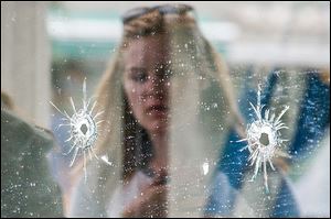 A woman looks at bullet holes on the window of IV Deli Mark on Saturday, where Friday night's mass shooting took place. 