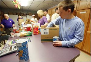 Volunteer Brett Griffis, fore, packs a box while other volunteers work on getting Nightingales Harvest food baskets together for delivery.