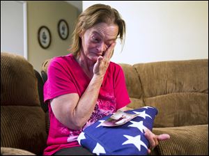 Vicky Olson wipes away a tear May 9 while talking about her husband, Michael Olson, a Marine veteran who died at home in their garage in March at age 45.  Vicky holds their wedding photograph , as well as a United States flag given to her at a memorial service for Michael. 