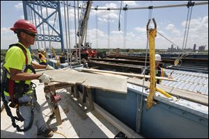 Eric Johnston, of Norwalk, passes a board to Marty Goon, of Genoa, right and partially obscured. Repair work is continuing and currently on time for the Anthony Wayne Bridge connecting east Toledo to Toledo.