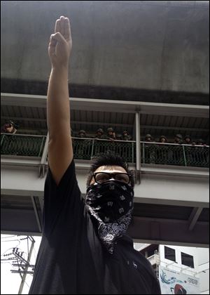 An anti-coup protester gives a three-finger salute as soldiers keep eyes on him from an elevated walkway near a rally site in central Bangkok, Thailand, Sunday.