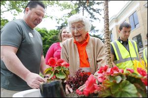 Trudy Price plants flowers with the help of Tracy Ricard, a licensed practical nurse, left, on the lawn of Bowling Green State University. She celebrated her 100th birthday on Monday.