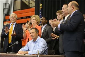 Surrounded by local school and public officials, including J. Robert Sebo, left, and BGSU President Mary Ellen Mazey, center left, Gov. John Kasich signs House Bill 484, a piece of educational legislation, before a group of hundreds of this year's Buckeye Boys State attendees at Bowling Green State University. 