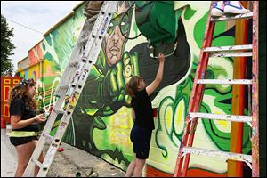 Bowling Green State University students Liz Butterfield, left, and Jamie Scherer, right, work alongside several other students Thursday on a mural on the side of the Green Lantern in South Toledo.