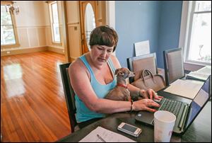 Velvet Bradley works part-time at the dining room table in her home, with her Italian greyhound, Sterling, in her lap, while editing a magazine in Rockmart, Ga. The living room behind her is empty because her house has been foreclosed on and she is in the process of moving out. 