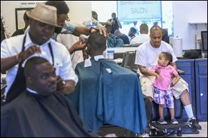Barber Devon Hands, Sr., right, helps his son Da’Mauri, 2, up into a spare chair at Hair Trendz Barbershop on Saturday. Free hair cuts were offered for fathers and sons to celebrate Father’s Day.